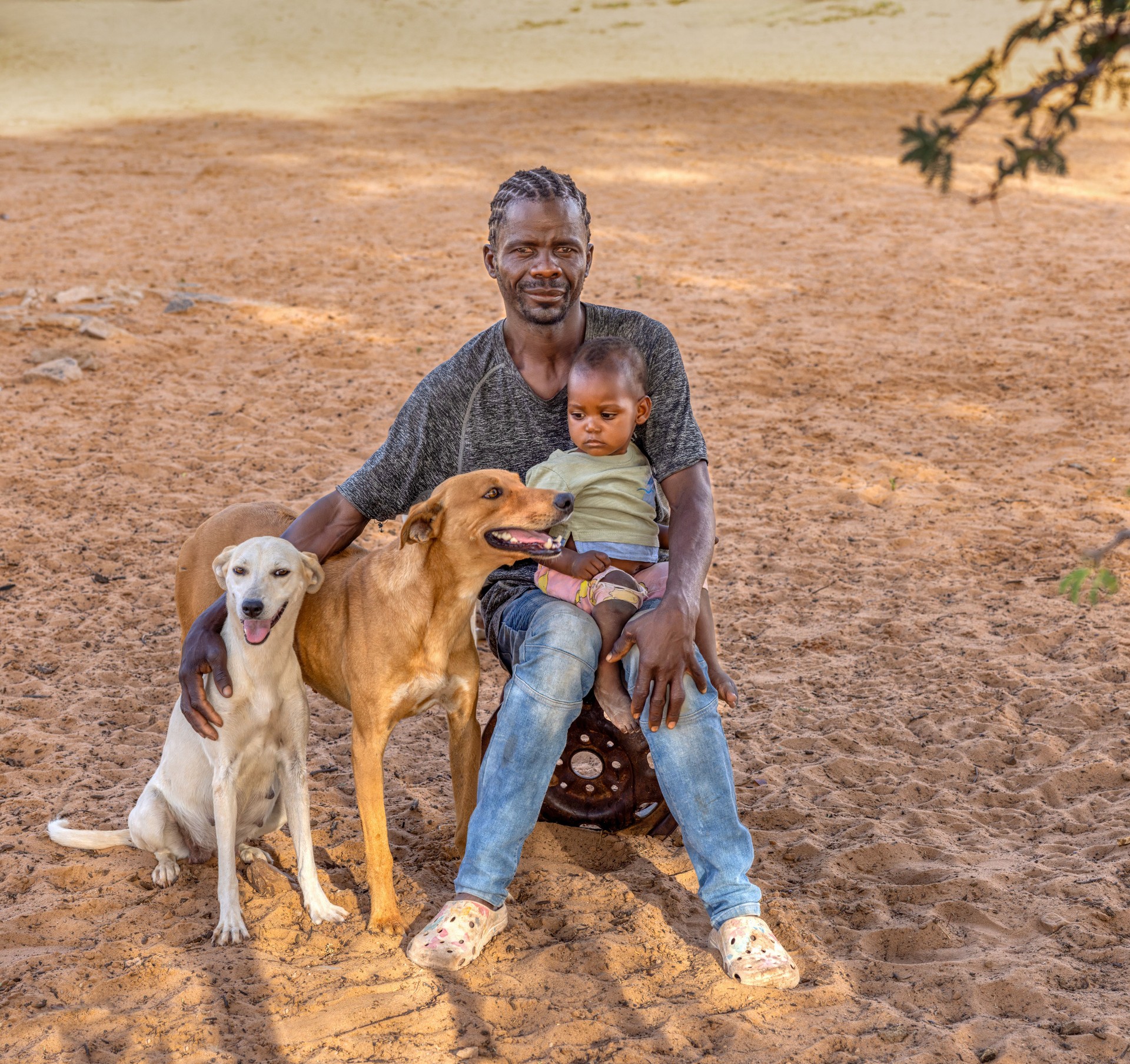 african village man with braids playing with his daughter and the two dogs